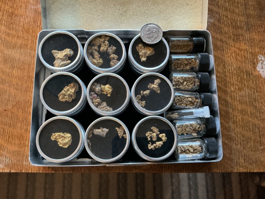Specimen jars of gold nuggets recovered from mining claims, shown next to a dime for scale